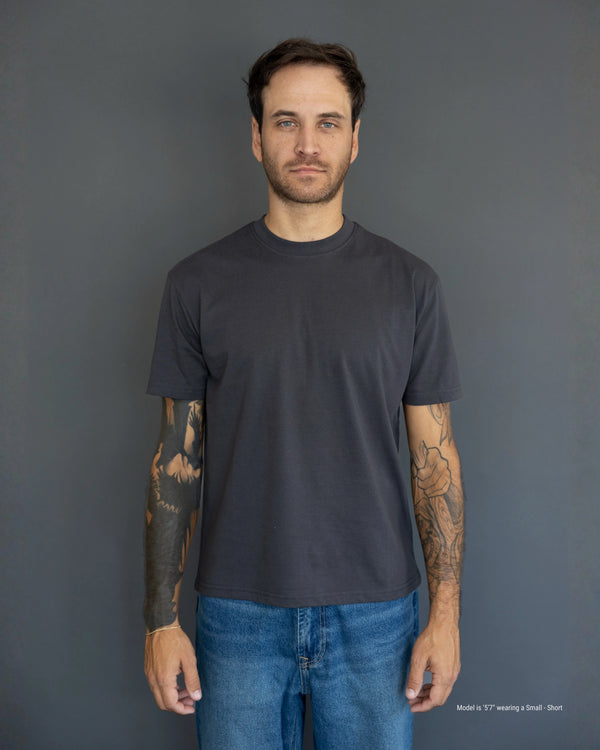 Shorter Man wearing a plain black t-shirt and blue jeans against a gray background