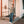 Load image into Gallery viewer, Person standing on a porch with a white door and red railing
