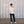 Load image into Gallery viewer, Shorter man wearing a white shirt and dark pants standing against a textured wall.
