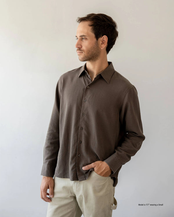 Man wearing a brown button-up shirt and beige pants against a plain background