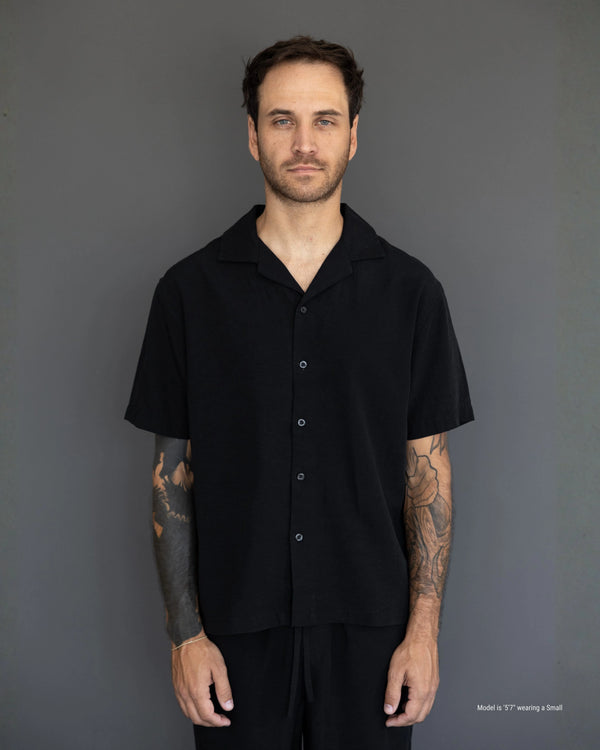 Man wearing a black short-sleeve button-up shirt against a gray background