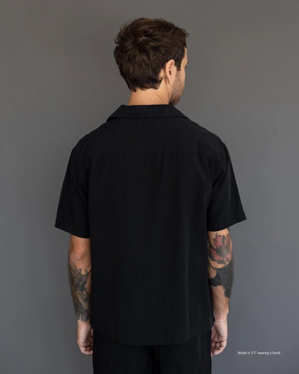 Man wearing a black short-sleeve shirt against a gray background