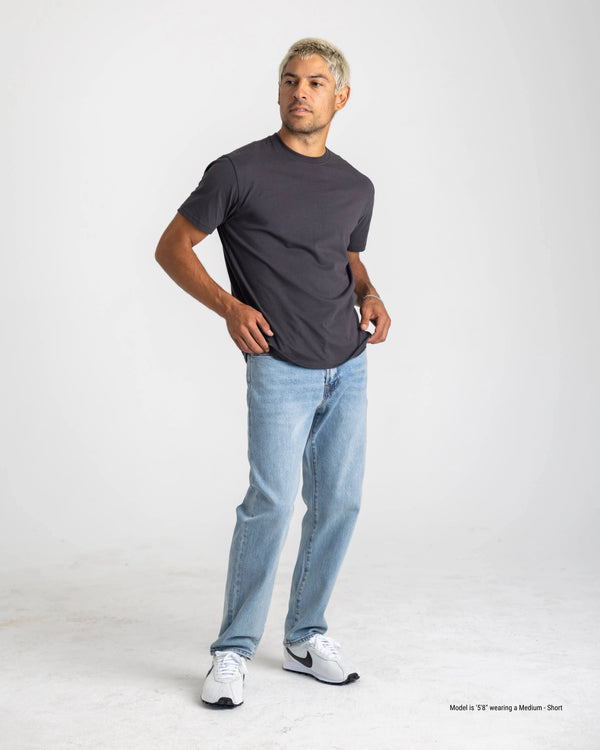Man wearing a dark gray t-shirt and light blue jeans on a white background
