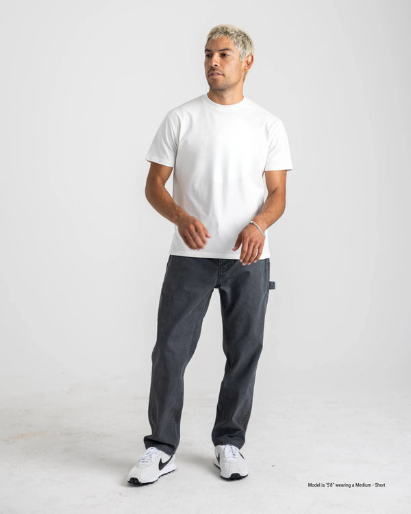 Man wearing a white t-shirt and dark pants on a plain background