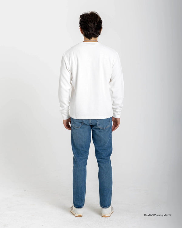 Short man wearing a beige checkered shirt and dark jeans on a white background