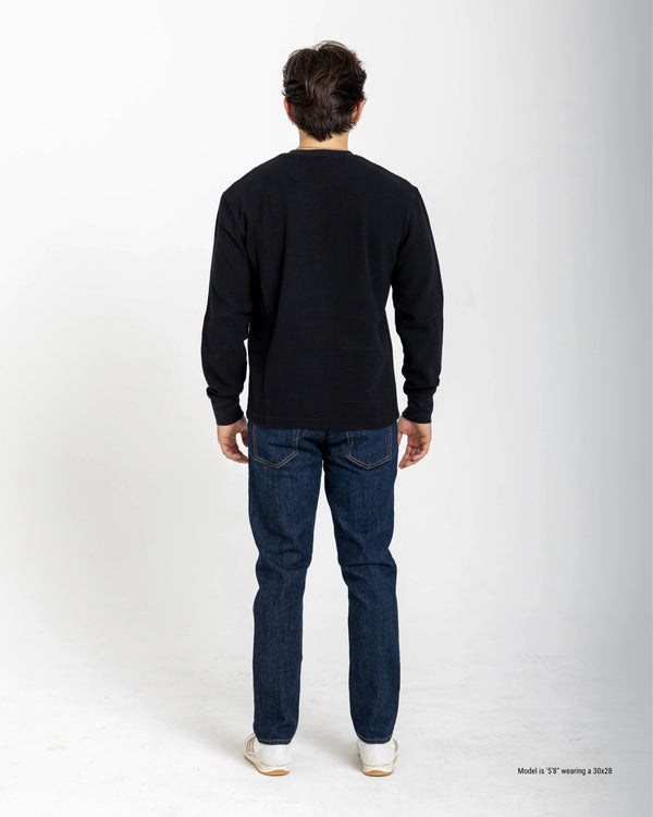 Person wearing a black long-sleeve shirt and blue jeans on a white background