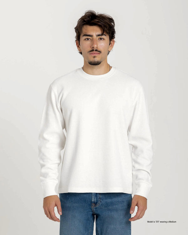 Man wearing a plain white long-sleeve shirt and blue jeans on a light gray background