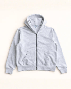 Man wearing a blue hoodie and gray pants standing in a minimalistic room.